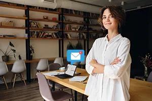 Imagem de mulher com braços cruzados com um notebook em cima de uma mesa em segundo plano